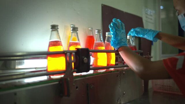 Quality control worker examining chia seed fruit juice bottles under light on conveyor belt in beverage factory for product inspection