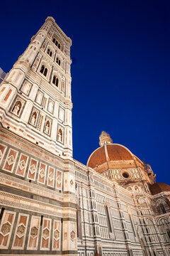 Florence Duomo at night. Illuminated cathedral marble facade and bell tower against deep blue sky.