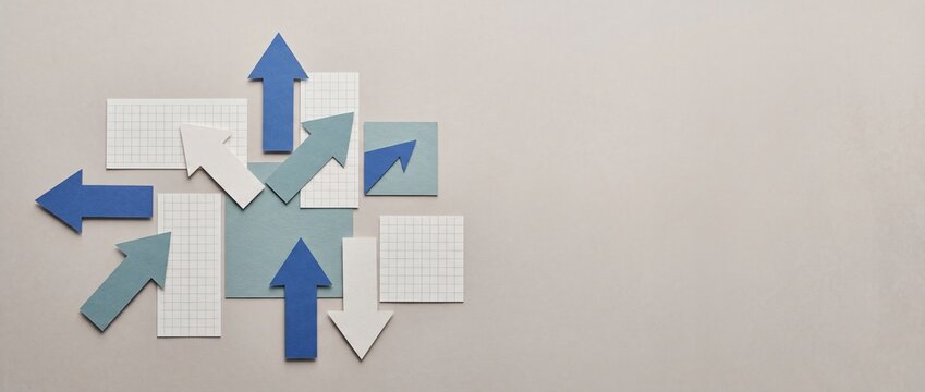 Paper arrows in blue white and teal pointing different directions on light gray background with copy space, business concept of strategy choice and direction.