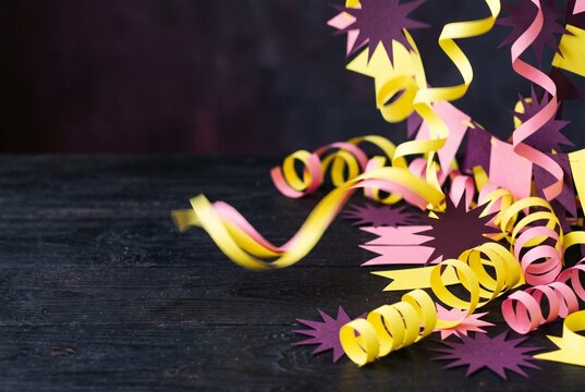 Curled yellow and pink paper streamers with purple starburst shapes on dark wooden surface, festive party decoration with copy space for celebration design.