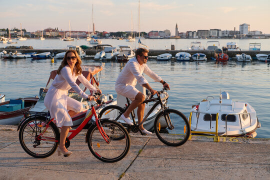 Couple Cycling Along Umag Harbor at Sunset With Boats and Romantic Waterfront Vibes