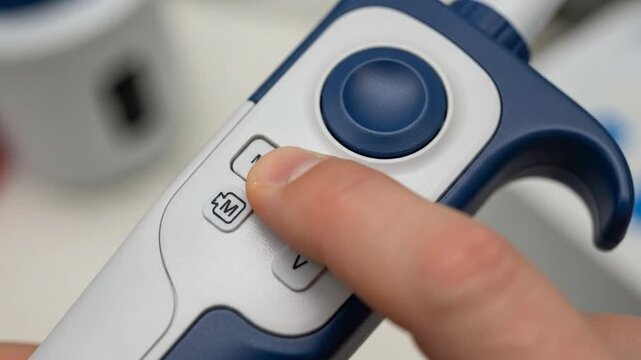 Close up of finger pressing buttons on electronic pipette in laboratory setting showing scientific