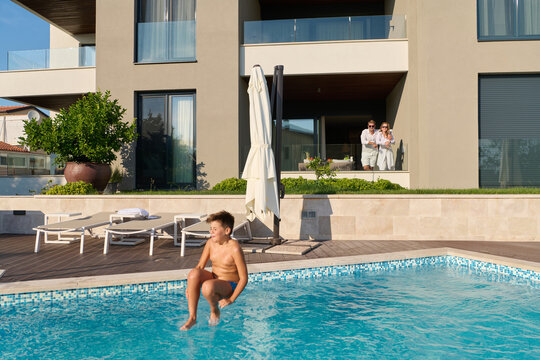 Family Enjoying Summer Poolside at Luxury Modern Home With Parents Watching From Balcony