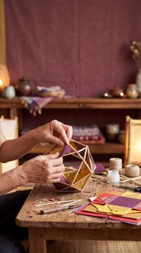Hands assembling handmade paper lantern from bamboo sticks and colorful sheets at wooden workshop table in warm lamplight, traditional festival craft.