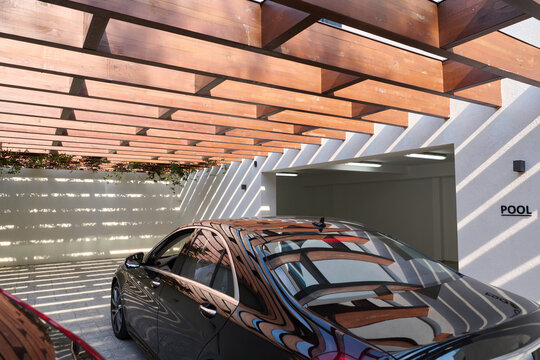 Modern Garage With Parked Car Under Wooden Pergola and Sunlit Pool Entrance