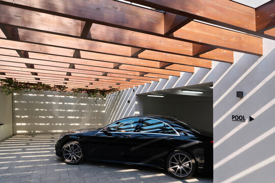 Luxury Black Sedan Parked Under Wooden Pergola Near Pool Entrance in Modern Garage