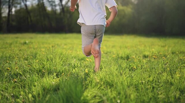 Child running in field. Child runs on the grass in a park. A kid lifestyle is running in the park. A kid sprinting across a meadow.