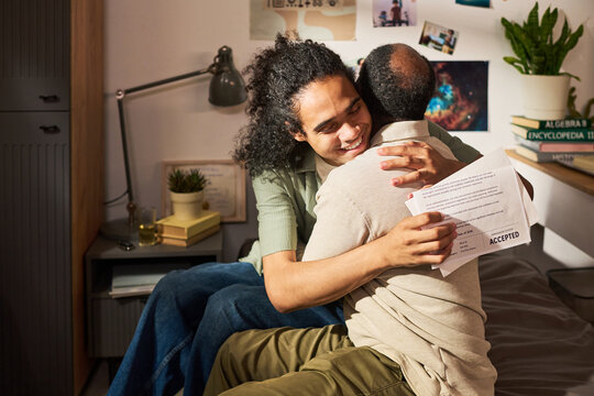 Father and son embracing while holding accepted college letter, celebrating academic success at home. Education marketing, scholarship campaigns, student achievement messaging
