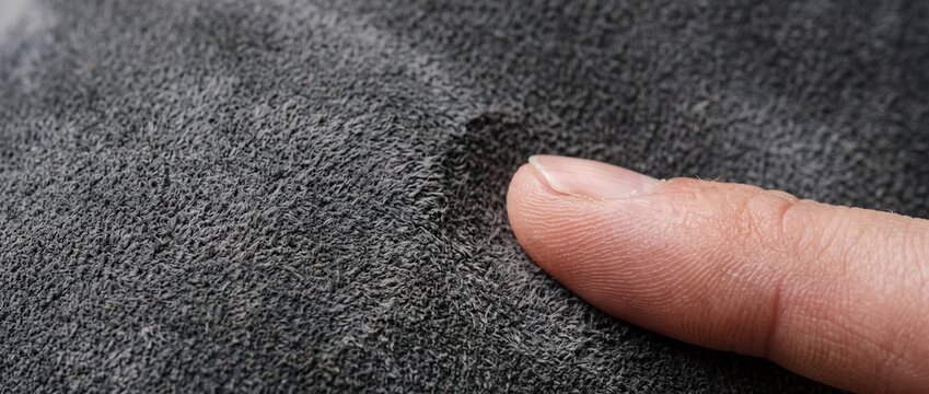 Fingertip touching soft dark grey suede fabric in extreme closeup showing napped texture and tactile quality of premium upholstery material.
