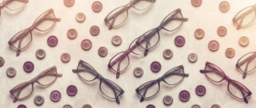 Vintage eyeglasses and assorted sewing buttons arranged in neat repeating rows on light beige textured background in muted retro tones for eyewear design.