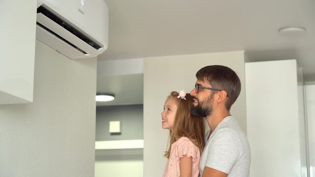 Father with little daughter turn on air conditioner using remote control. Happy family adjust comfortable temperature on air conditioner.