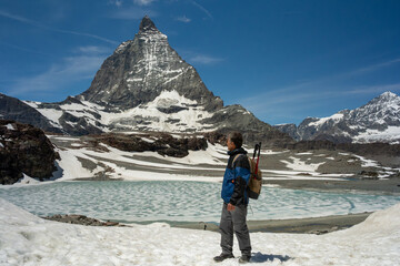Naklejka premium Hiker admiring the iconic matterhorn mountain on a sunny day near a partially frozen alpine lake