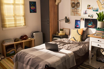Obraz na płótnie Canvas Wide angle shot of student bedroom featuring laptop on bed, study desk, books, suitcase, personal decor, suggesting college living, remote learning, youth lifestyle marketing