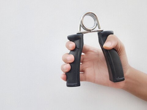 Hand squeezing a black hand gripper for grip strength training and forearm exercise on plain background with copy space.