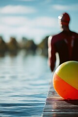 Fototapeta premium Man swimmer standing on wooden dock with inflatable ball near lake. Athlete preparing for triathlon training in water. Sports concept, outdoor fitness activity, endurance exercise.
