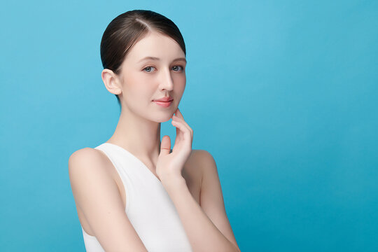 A beautiful young Asian woman with clean, fresh skin against a blue background. Skincare, facial treatment, cosmetology, beauty, and spa. An elegant portrait of an Asian woman.