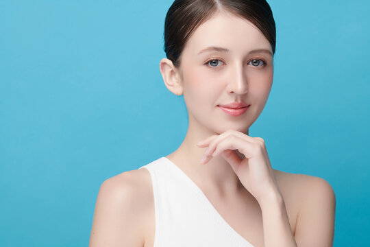 A beautiful young Asian woman with clean, fresh skin against a blue background. Skincare, facial treatment, cosmetology, beauty, and spa. An elegant portrait of an Asian woman.
