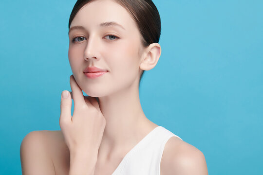 A beautiful young Asian woman with clean, fresh skin against a blue background. Skincare, facial treatment, cosmetology, beauty, and spa. An elegant portrait of an Asian woman.