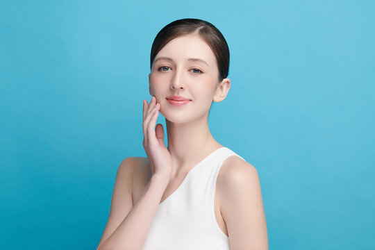 A beautiful young Asian woman with clean, fresh skin against a blue background. Skincare, facial treatment, cosmetology, beauty, and spa. An elegant portrait of an Asian woman.