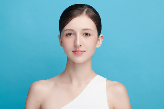 A beautiful young Asian woman with clean, fresh skin against a blue background. Skincare, facial treatment, cosmetology, beauty, and spa. An elegant portrait of an Asian woman.