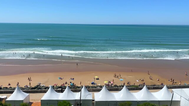 White event tents set up along the promenade overlooking surfers catching waves at Plage de la C&ocirc;te des Basques in Biarritz, France
