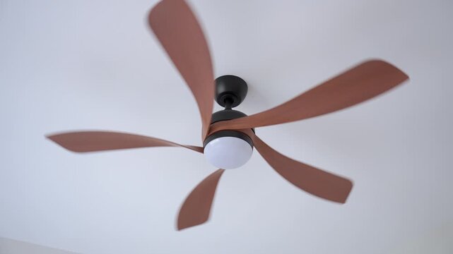 Person uses remote control to operate ceiling fan mounted on ceiling inside modern home. Concept of home cooling and energy efficient climate control