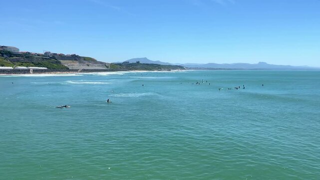 Wide panoramic view of surfers scattered in the ocean swell off Plage de la C&ocirc;te des Basques with the Pyrenees in the background in Biarritz, France