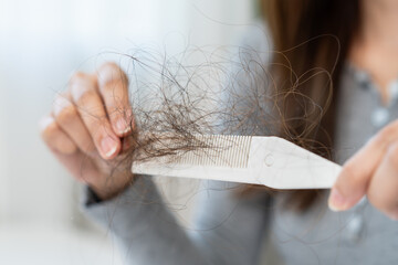 Hair fall problem concept. Shocked Asian woman looking at many hair lost in her hand and comb.