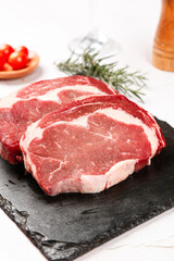 Fototapeta premium Fresh Raw Ribeye Steaks on Slate Board with Rosemary - Premium Thick Cut Beef Ready for Cooking