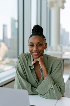 Closeup professional portrait of a smiling woman in a green blouse by large windows for business profile and website background