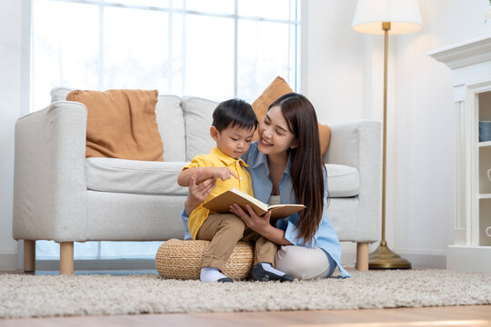 Asian Mother Reading Book to Her Little Son in Living Room