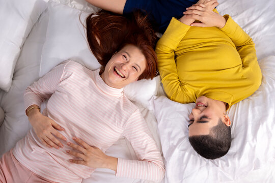 Happy Lesbian Couple Lying on Bed Together and Laughing