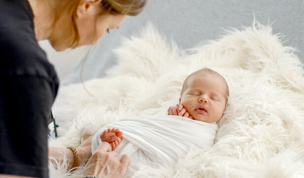 Professional photographer gently wraps tiny sleeping infant in soft white blanket at home studio