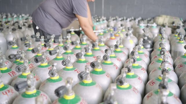 Worker checking rows of scuba diving aluminum air tanks in a warehouse for inspection and refilling