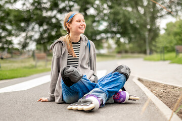 Obraz premium Blonde girl rests on park path. Wears rollerblades, protective gear.