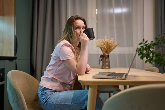 Woman taking coffee break while working on laptop at home