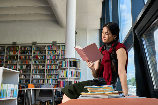 Smart young woman immersed in books at college library on campus
