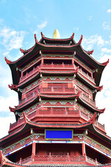 Fototapeta premium Traditional Red Chinese Pagoda Tower with Upturned Eaves Against Blue Sky
