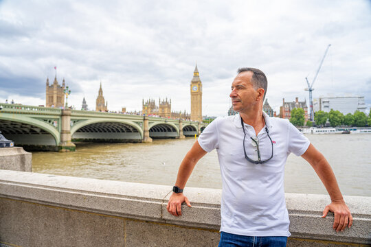 A white European man in a white shirt is in London. A white European man in a white shirt is in London in the background of Big Ben and the bridge.
