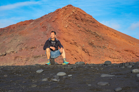 A white European man stands before the red mountain in Lanzarote, Canary Islands, Spain.