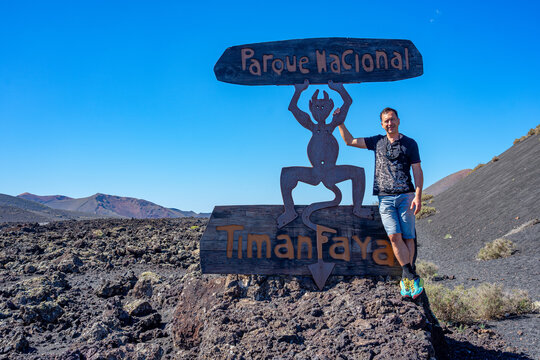 A white European man stands near an information sign for Timanfaya National Park in Lanzarote, Canary Islands, Spain.
