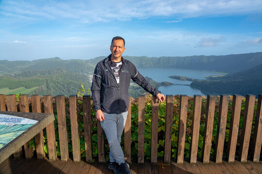 A white European man in a black coat at the viewpoint of the Sete Cidades lagoon, S&atilde;o Miguel Island.