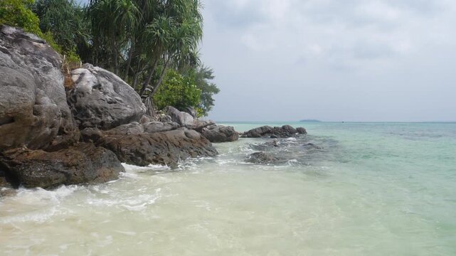 Slow motion: waves on rocky tropical shoreline with crystal clear turquoise sea in Karimunjawa National Park Indonesia lush vegetation and tranquil island scenery