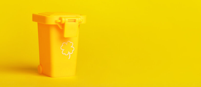 Minimalist yellow recycling bin with clover symbol, isolated on vibrant yellow background, concept for eco-friendly waste management.
