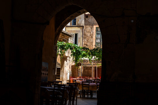 Through a dark stone archway, you can catch a glimpse of a typical Sicilian open-air trattoria basking in the sunshine