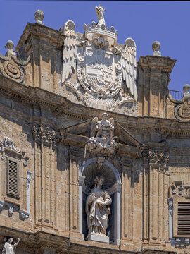 Vertical view of ornate Baroque architecture at Quattro Canti in Palermo, Sicily, highlighting weathered marble statue of a Spanish King nestled in decorative niche beneath a heraldic coat of arms.