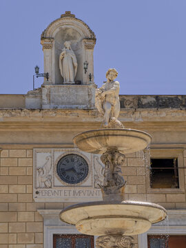 A beautiful vertical view of the fountain at Piazza Pretoria in Palermo, Sicily, featuring a marble cherub statue sparkling with water droplets against the historic Palazzo Pretorio clock tower.