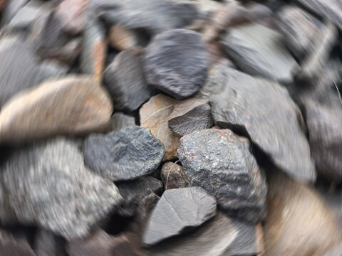 Abstract radial zoom motion blur on crushed dark gravel and basalt rocks, close-up overhead view