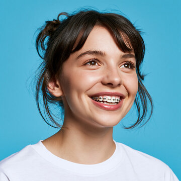 Retrato de uma jovem mulher feliz sorrindo com aparelho ortod&ocirc;ntico nos dentes, olhando para cima, fundo azul