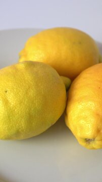 Three lemons sit on a plate in good light. vertical video